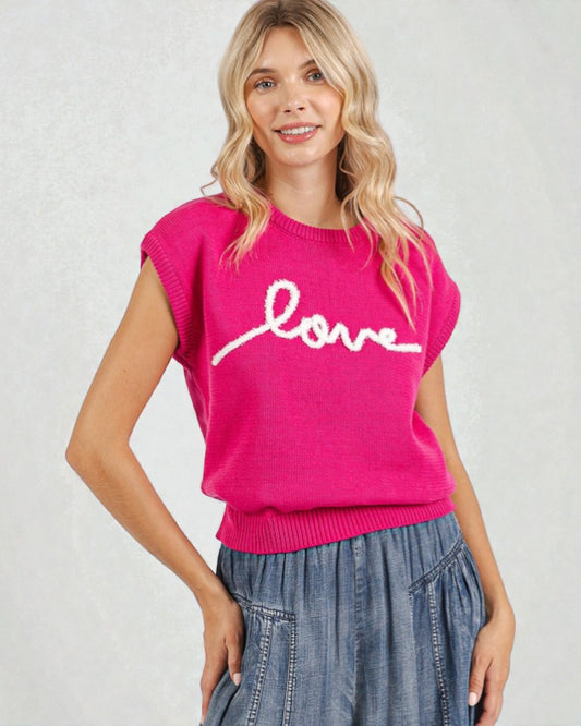 Woman wearing a pink sweater with 'love' on it against a plain background