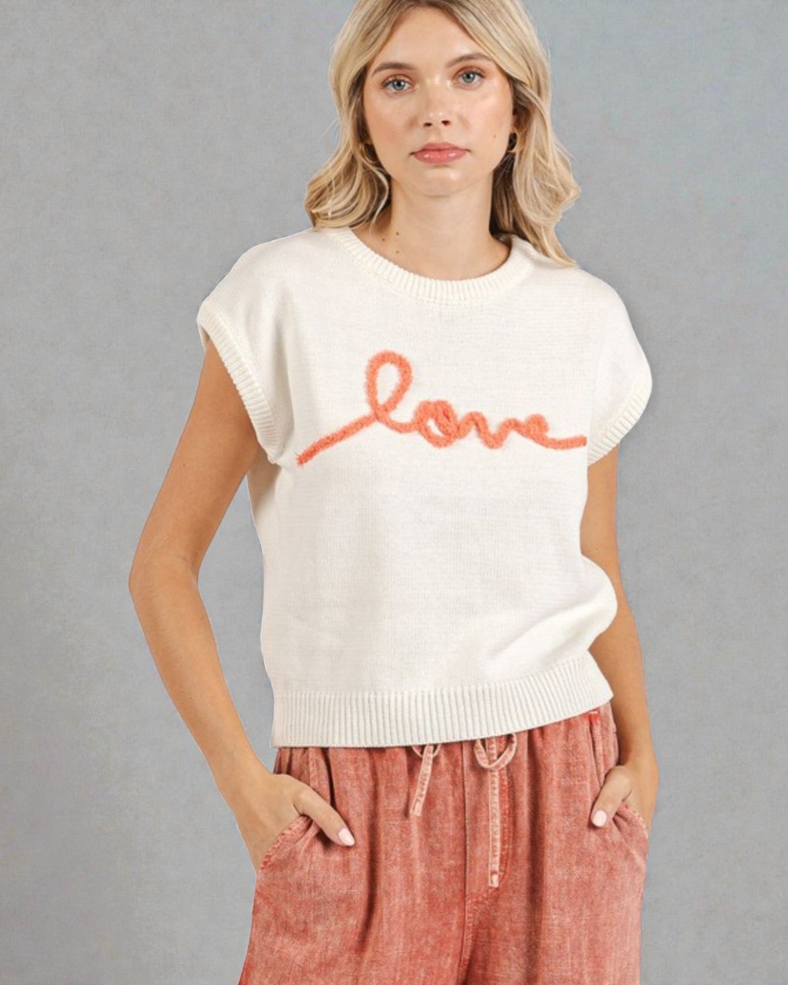 Woman wearing a white sweater with 'love' printed on it against a gray background