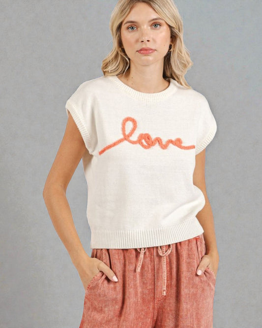 Woman wearing a white sweater with 'love' printed on it against a gray background
