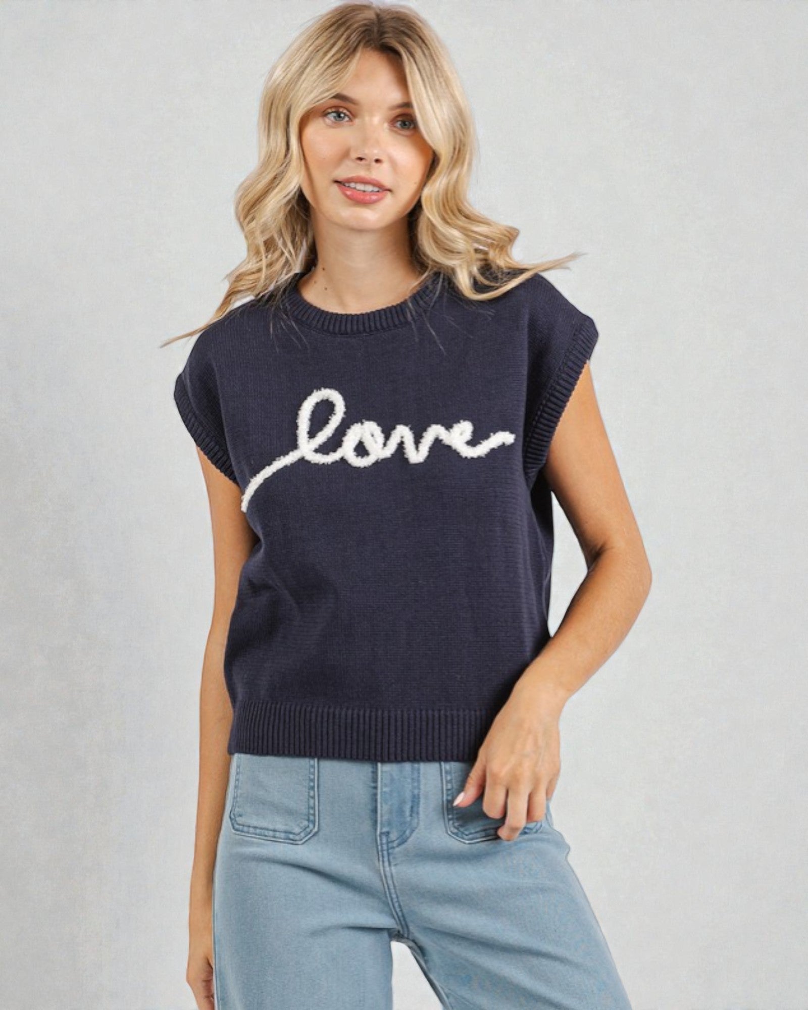 Woman wearing a navy sleeveless sweater with 'love' text on a light gray background