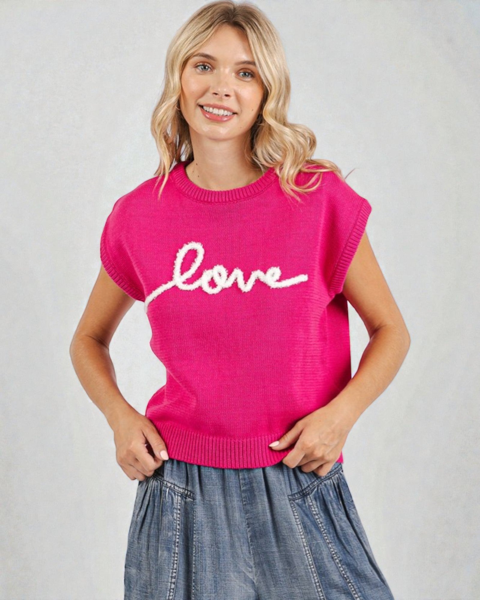 Woman wearing a pink sweater with 'love' on it against a plain background