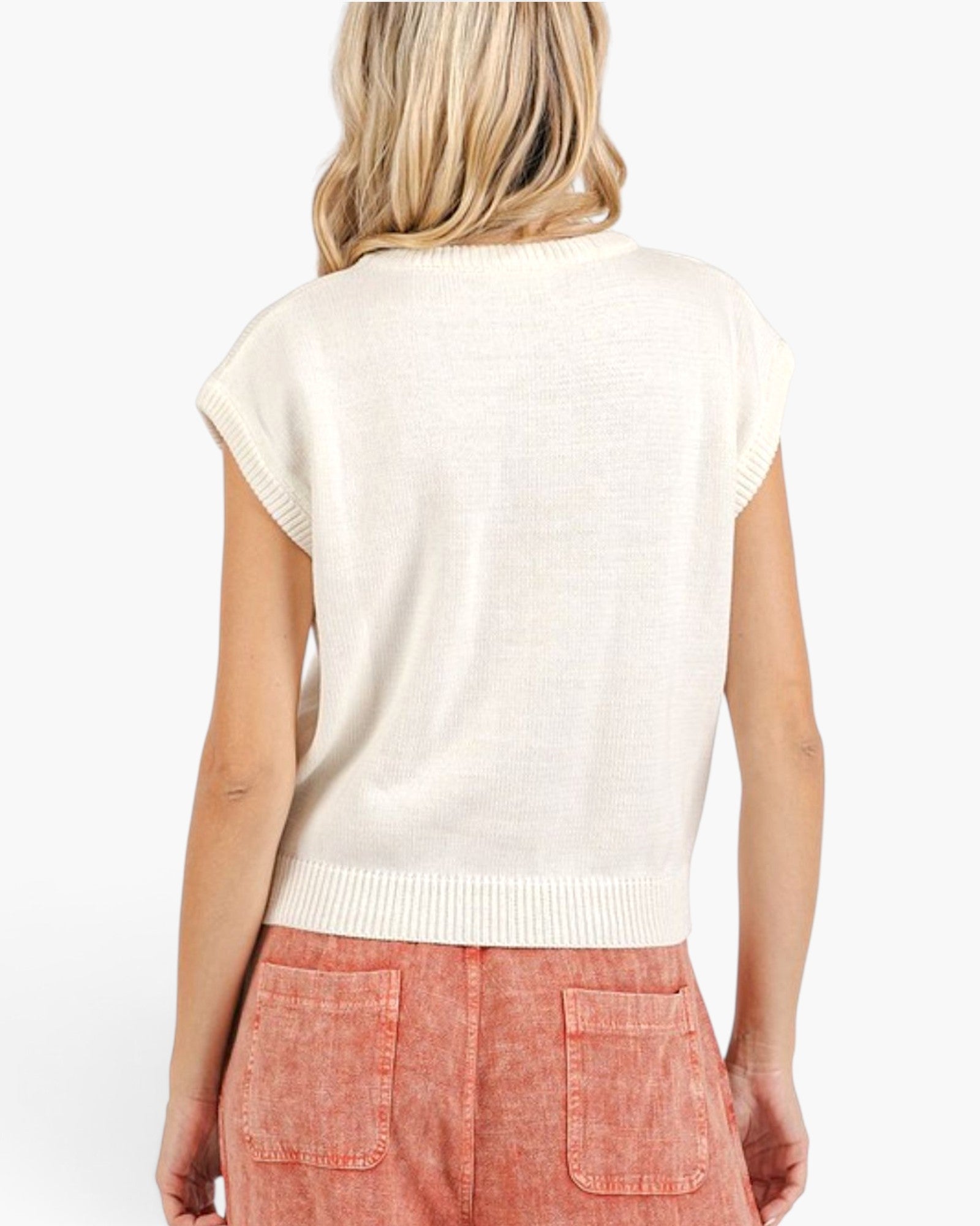 A woman shown from the back wearing a cream-colored, short-sleeve ribbed knit sweater and coral pink pants against a plain white background.