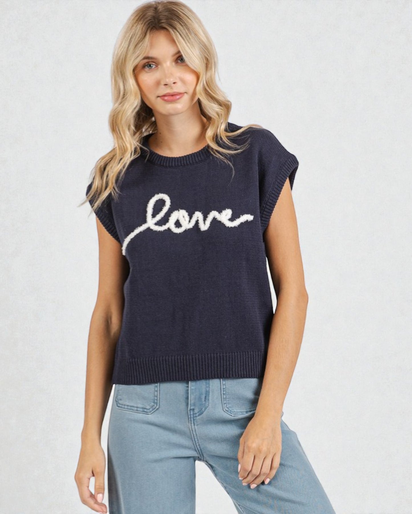 Woman wearing a navy sleeveless sweater with 'love' text on a light gray background