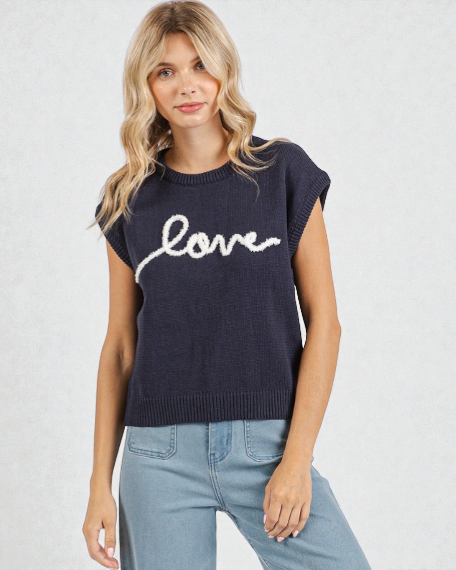 Woman wearing a navy sleeveless sweater with 'love' text on a light gray background