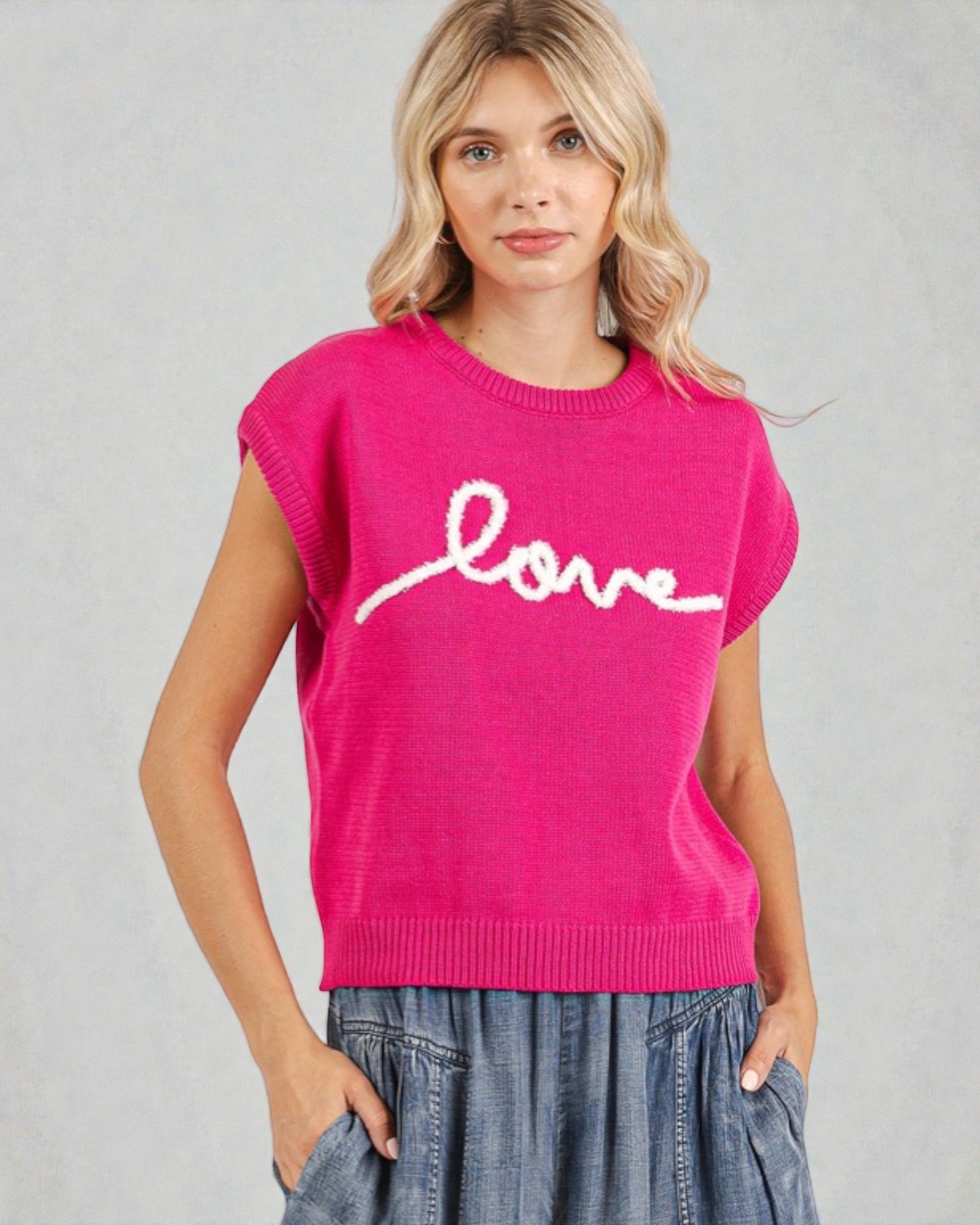 Woman wearing a pink sweater with 'love' printed on it against a gray background