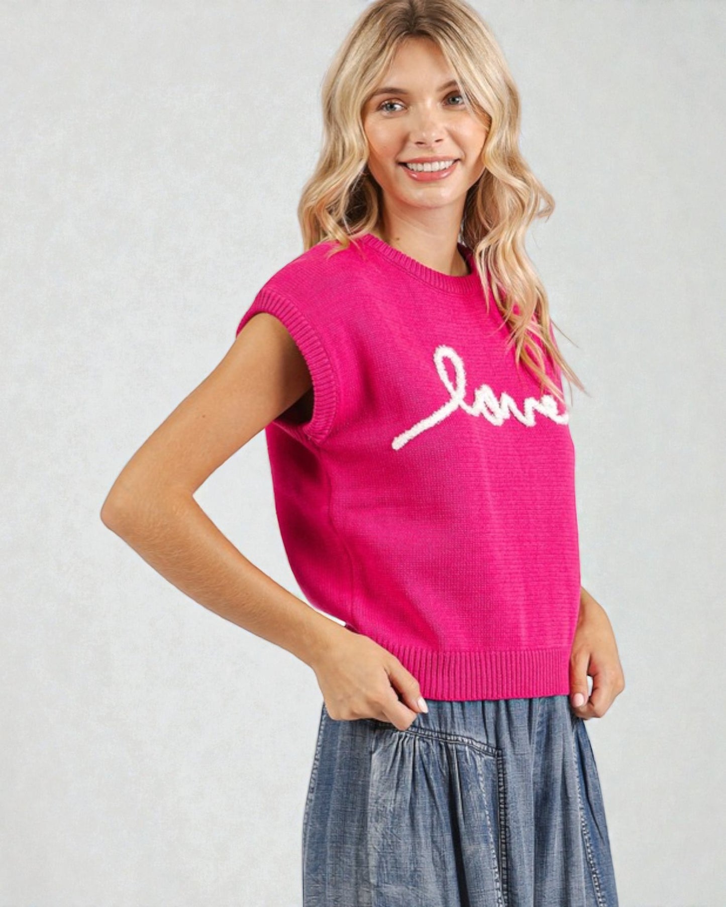 Woman wearing a pink sleeveless sweater with 'love' on it against a light background
