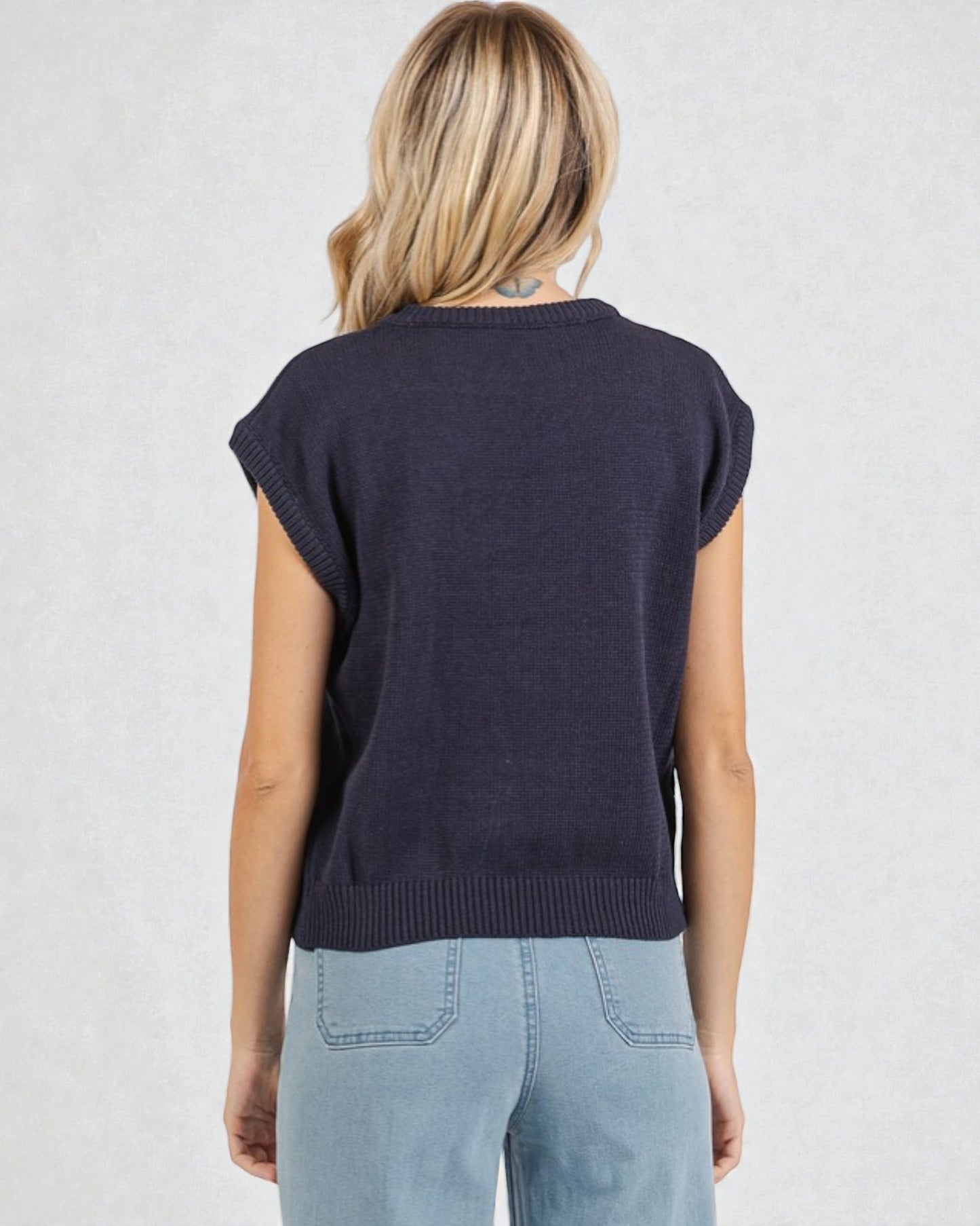 Person wearing a navy sleeveless sweater against a light background