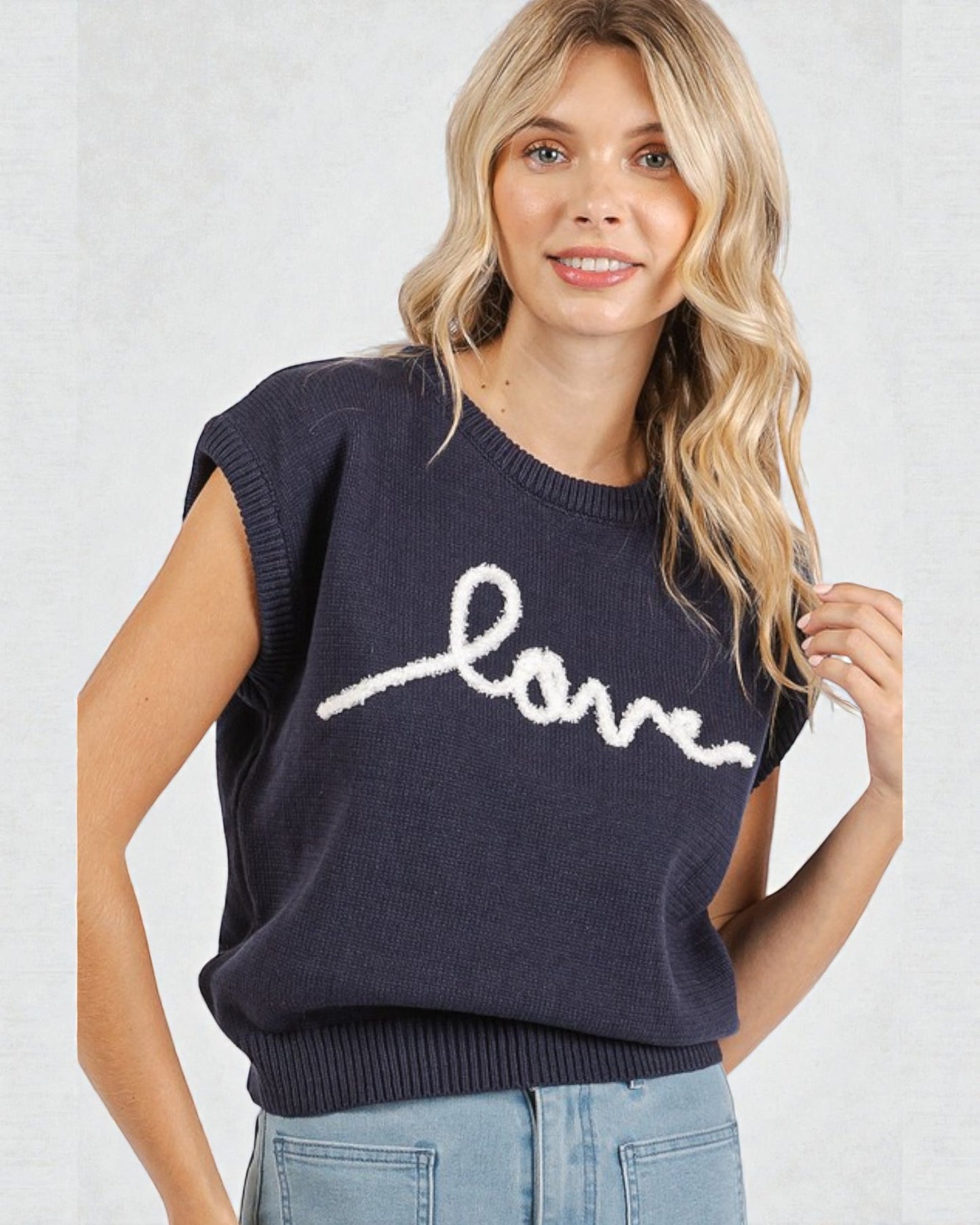 Woman wearing a navy sweater with 'love' written on it against a white background