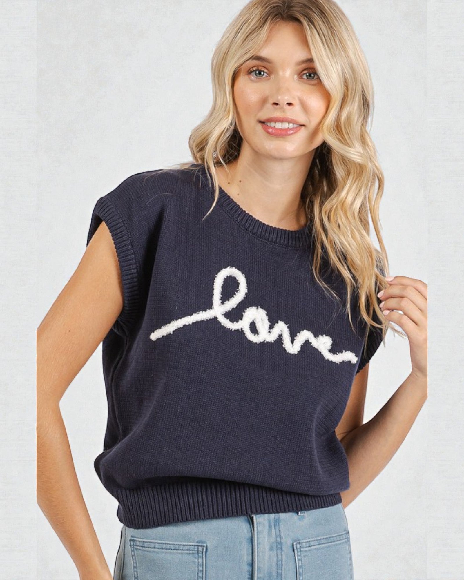 Woman wearing a navy sweater with 'love' written on it against a white background