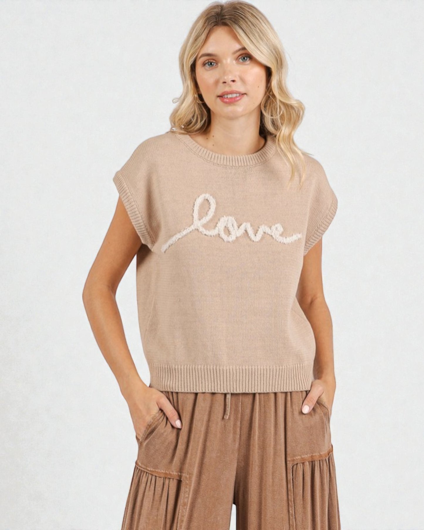 Woman wearing a beige sleeveless sweater with 'love' text on a white background