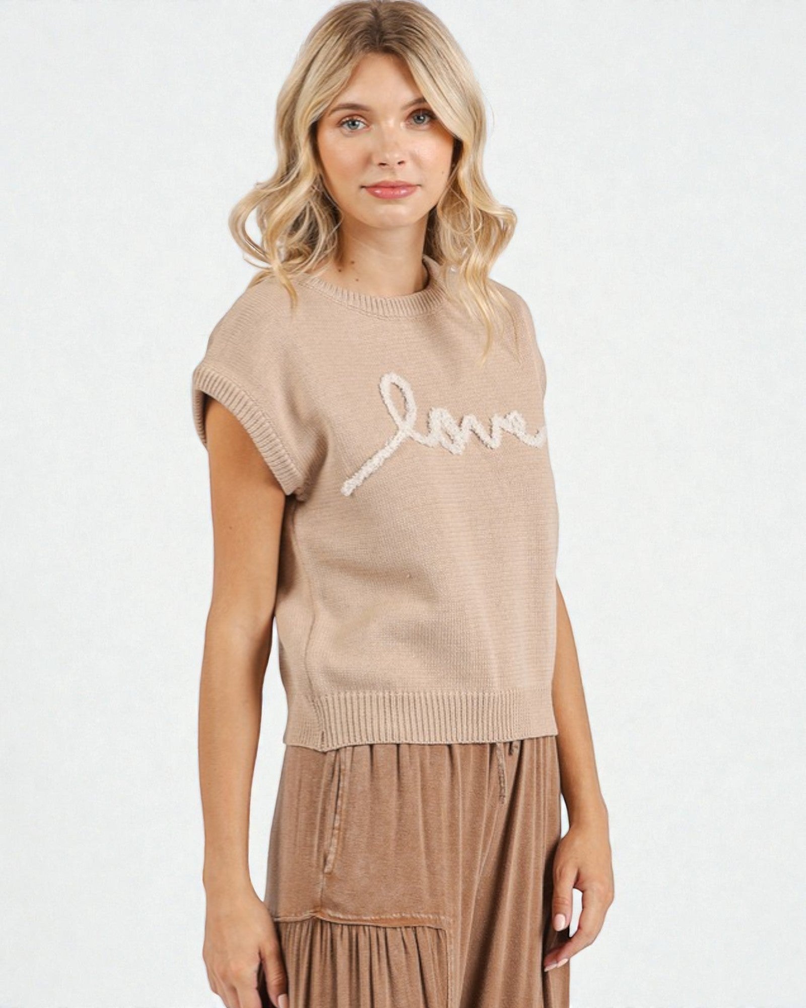 Woman wearing a beige knit sleeveless top with 'love' text on a white background
