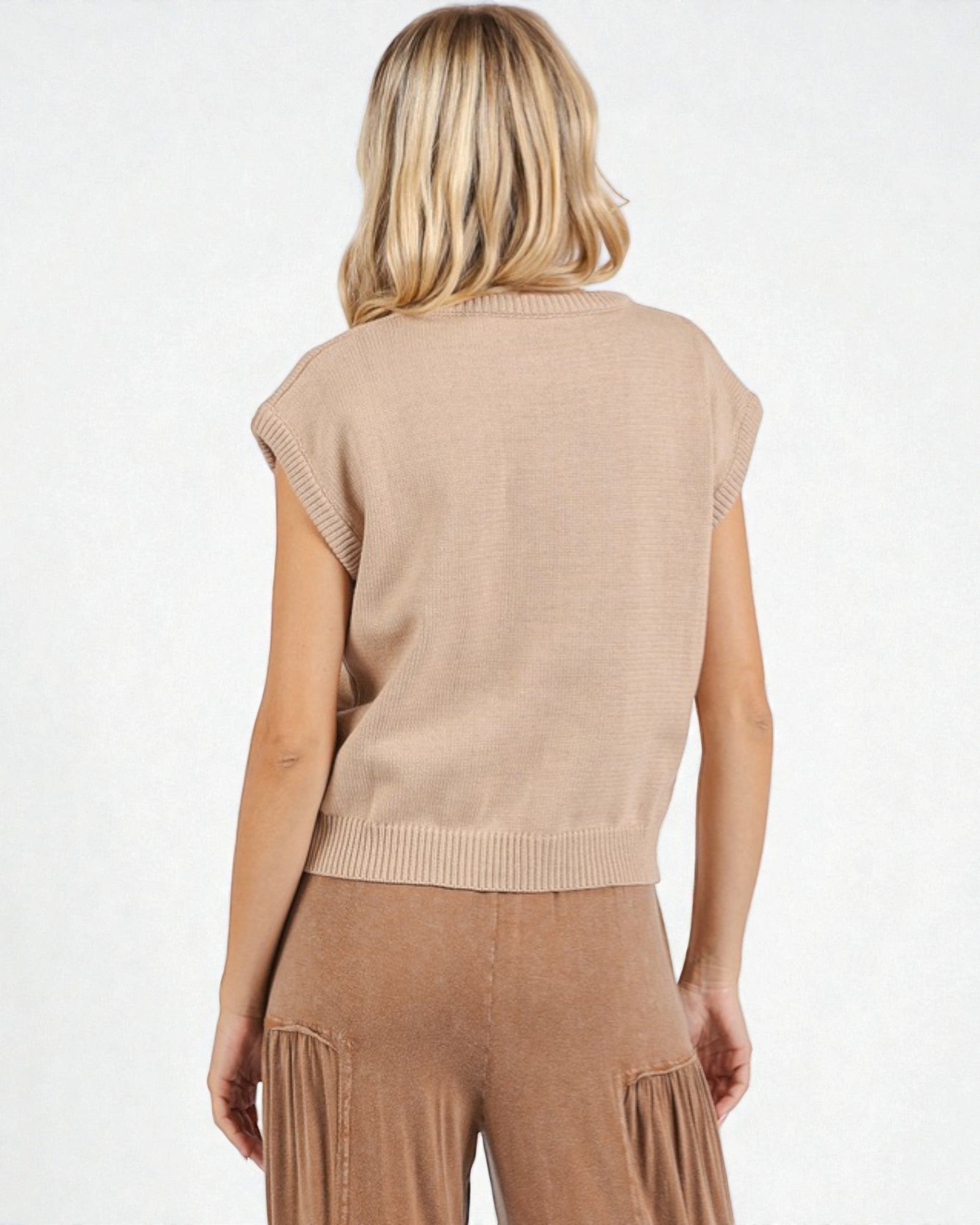 Woman wearing a beige knit vest and pants on a white background