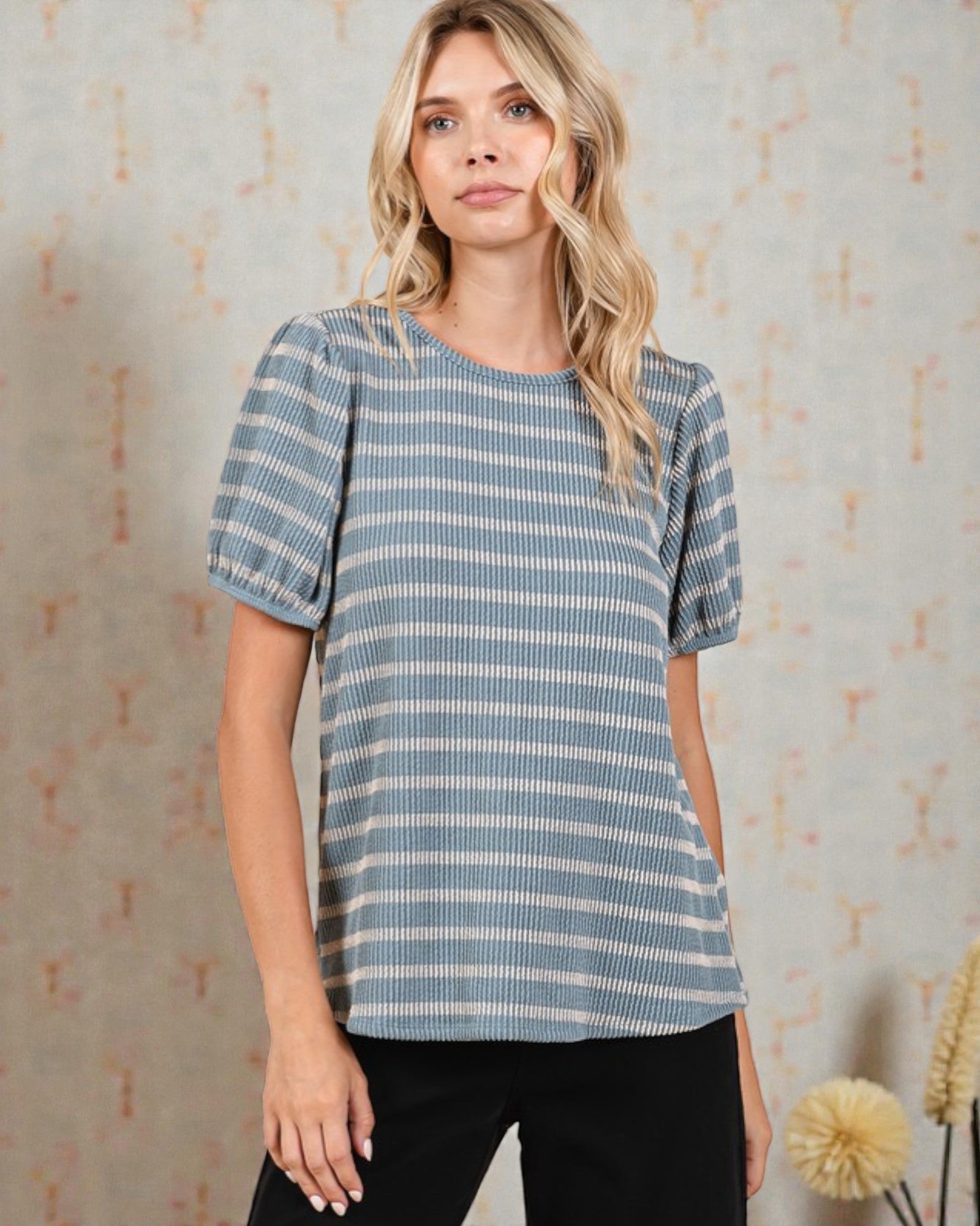 Woman wearing a blue and white striped shirt against a textured wall.