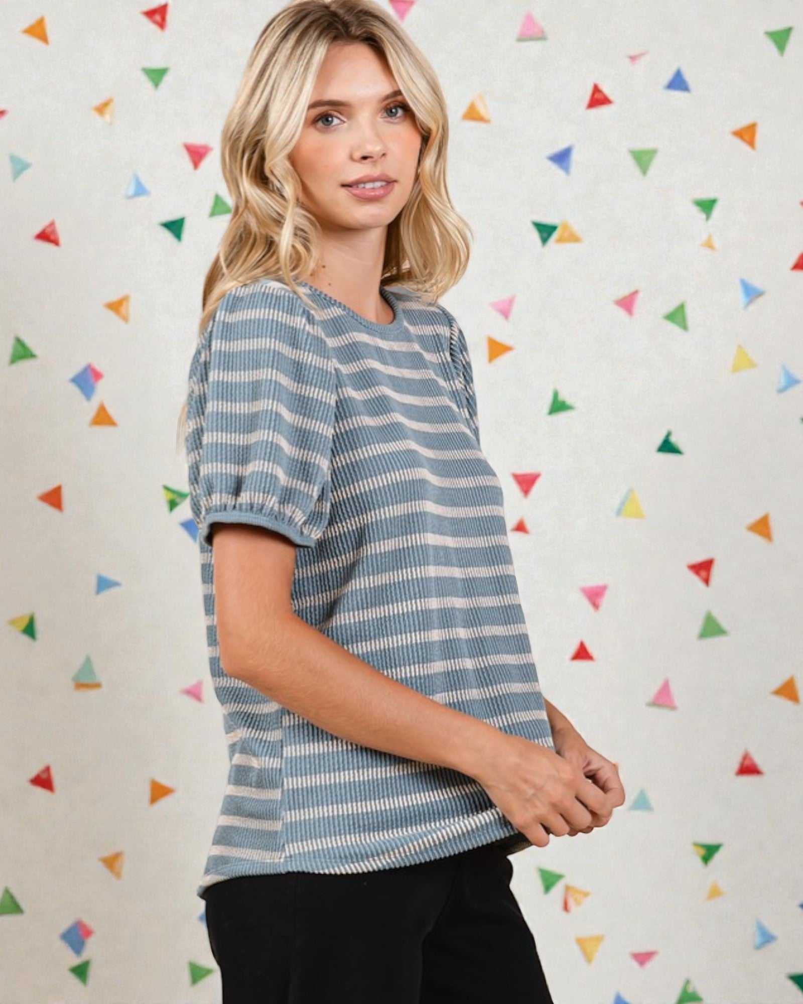 Woman wearing a striped shirt against a colorful geometric-patterned wall.