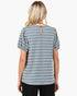 A woman viewed from the back wearing a short-sleeve top with vertical blue and off-white stripes, a small keyhole cutout at the back neckline, and puff sleeves. She is also wearing black pants against a plain light gray studio background.