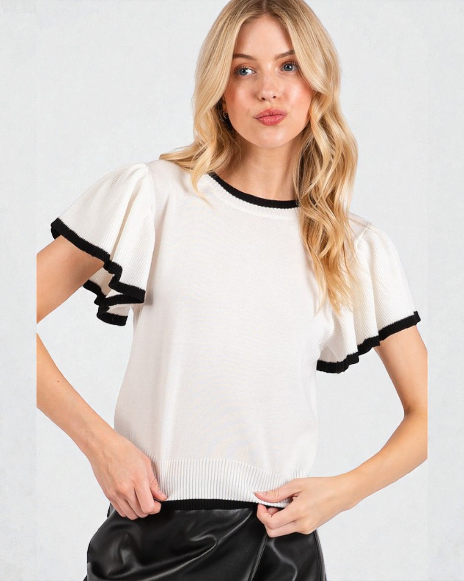 Woman wearing a white sweater with black accents on a plain background