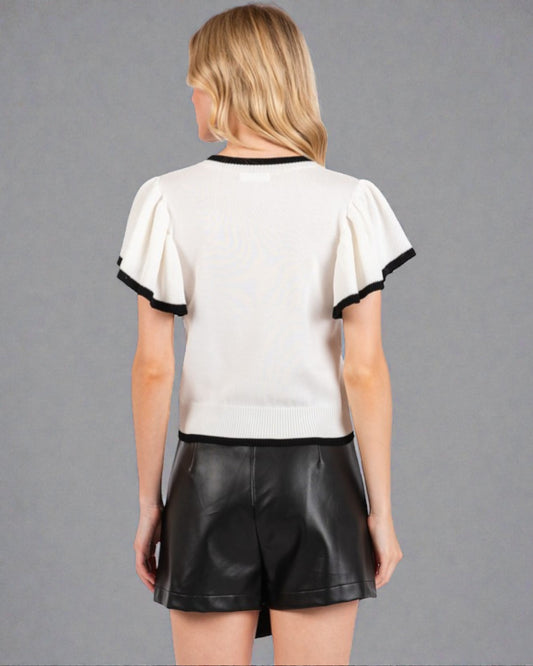 Woman wearing a white blouse with black trim and black shorts on a gray background