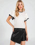 Woman wearing a white blouse with black trim and a black leather skirt on a light gray background