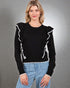 Woman wearing a black sweater with white ruffle details on a gray background