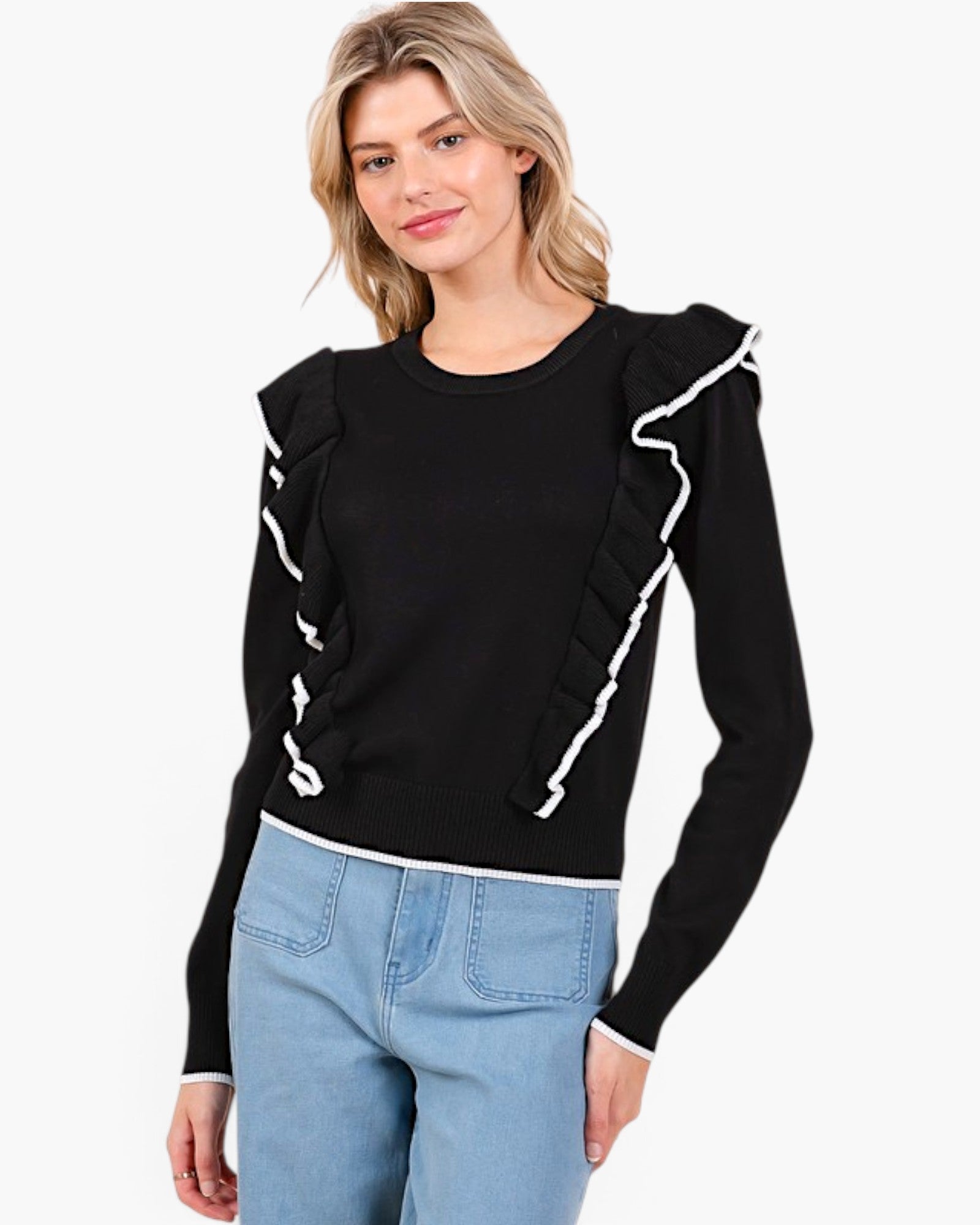 A woman wearing a black long-sleeve knit sweater with white ruffle trim details on the shoulders and sides, paired with light blue jeans, against a plain white background.