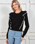Woman wearing a black sweater with ruffled sleeves against a white wooden door background