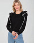 Woman wearing a black sweater with white ruffle details on a plain background