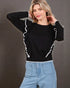Woman wearing a black sweater with white trim and light blue jeans against a gray background