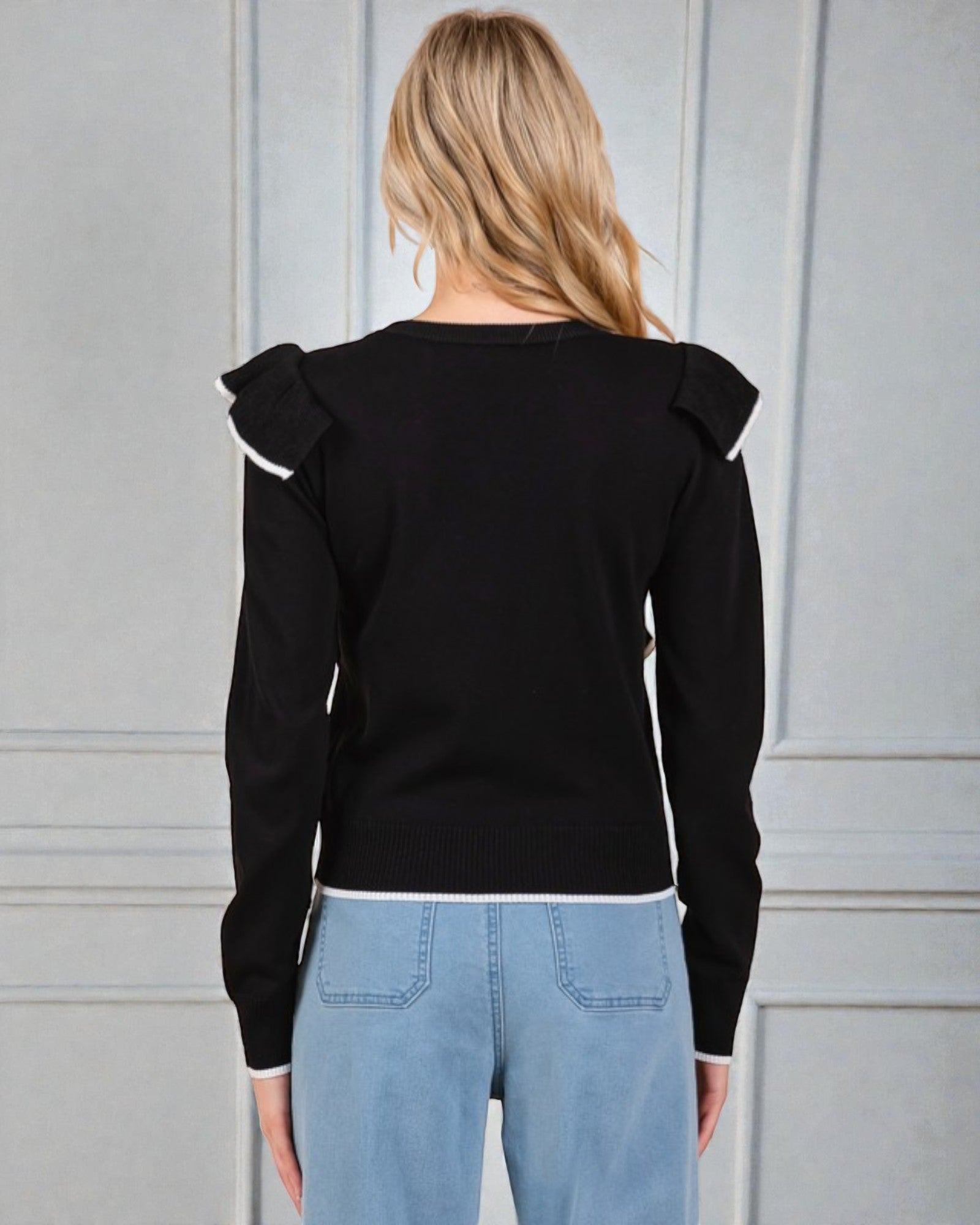 Person wearing a black sweater with ruffled shoulders against a gray background