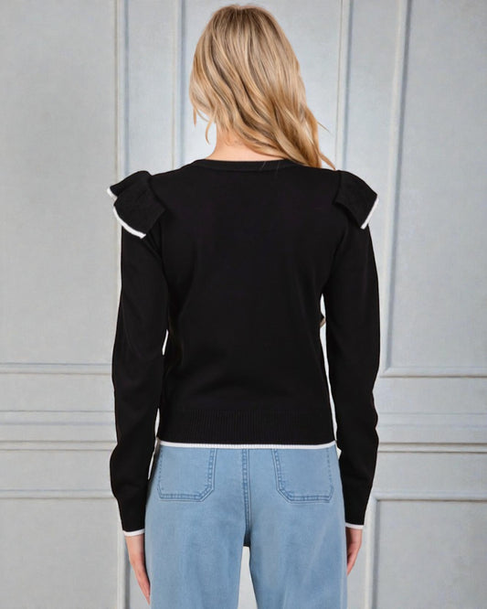 Person wearing a black sweater with ruffled shoulders against a gray background