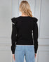 Person wearing a black sweater with ruffled shoulders against a gray background