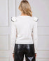 Person wearing a white blouse with black trim and black leather pants against a light-colored wall.