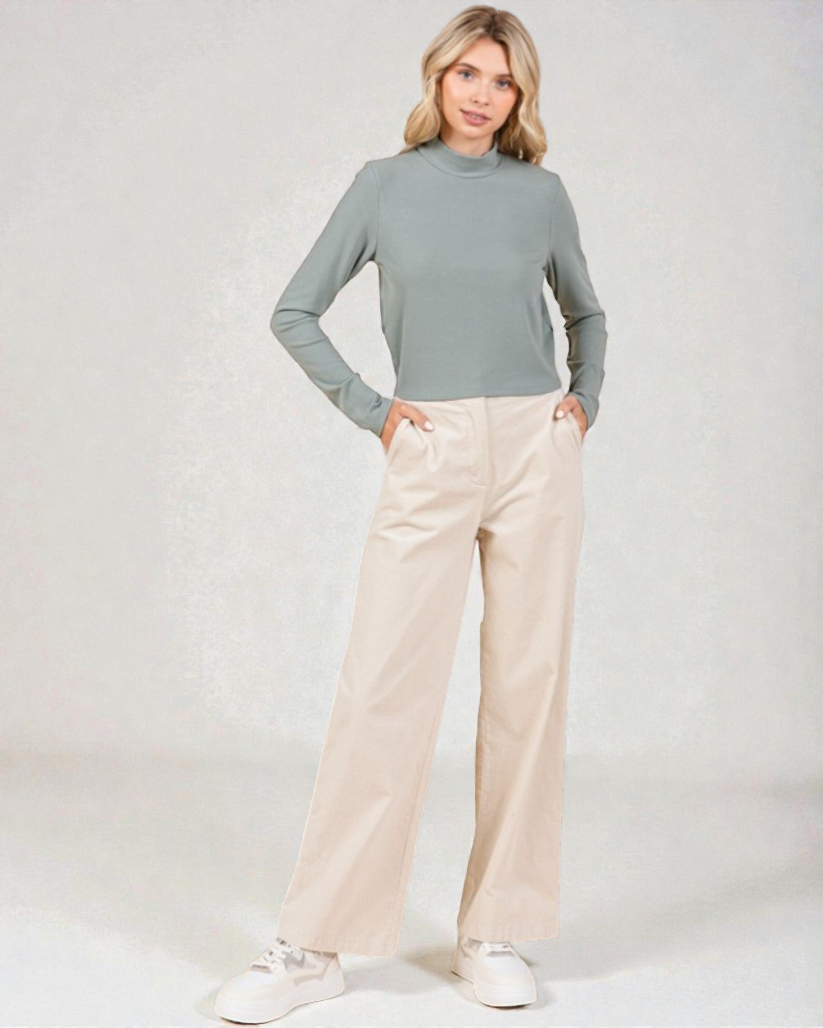Woman wearing a green turtleneck and beige pants on a white background