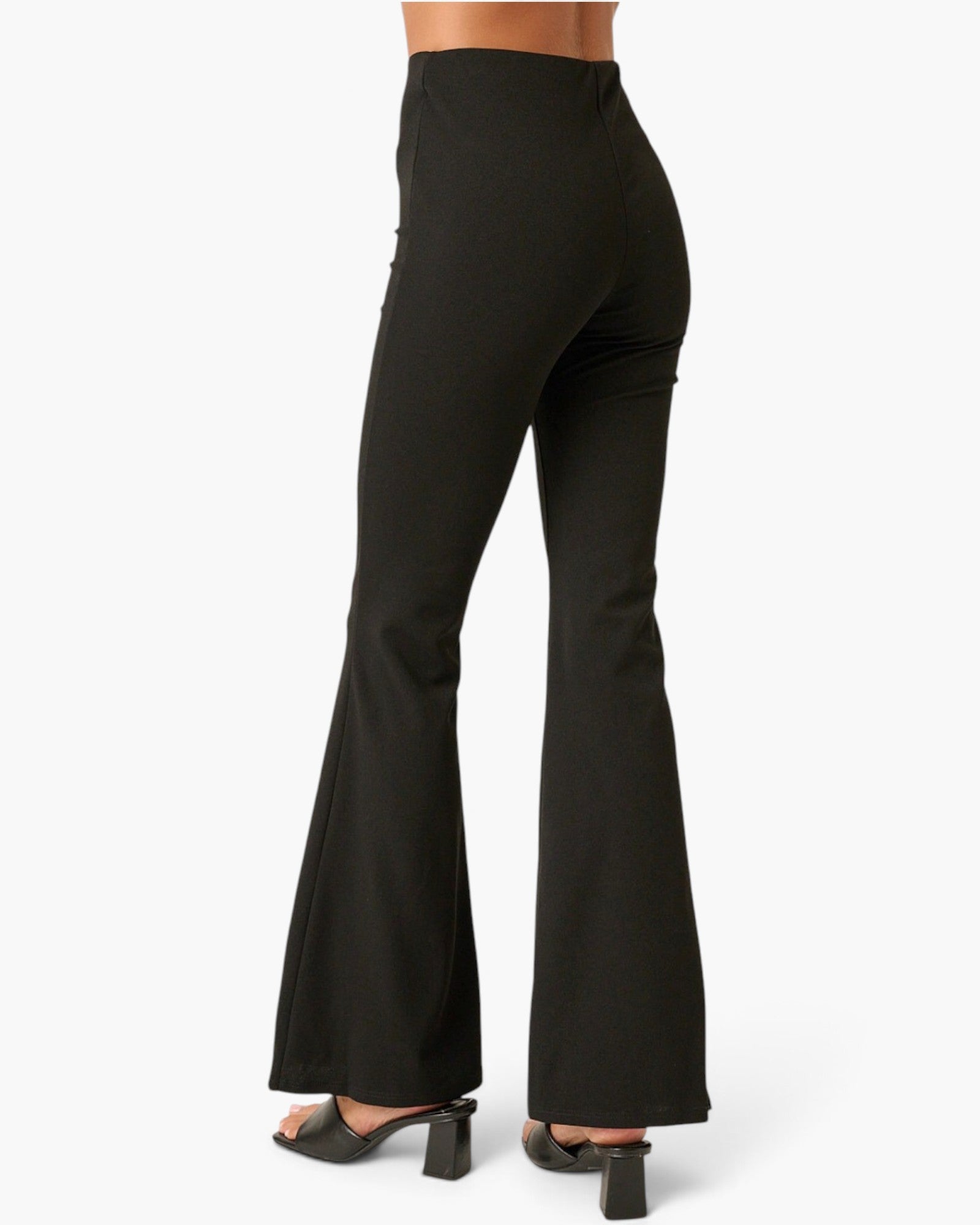 Black high-waisted flared pants shown from the back on a model, paired with black block-heel mules, against a plain white studio background.