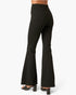 Black high-waisted flared pants shown from the back on a model, paired with black block-heel mules, against a plain white studio background.