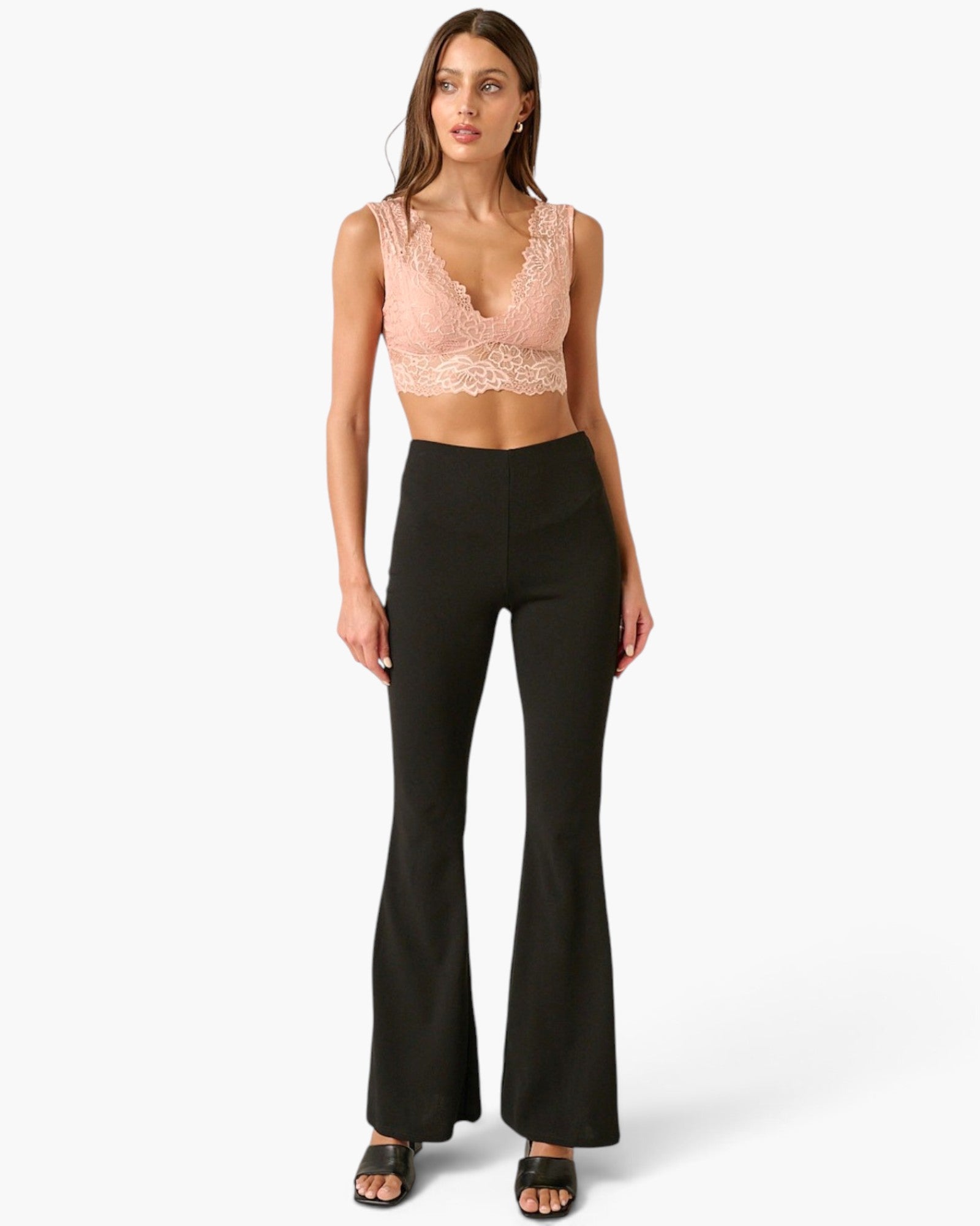 A model wearing a light pink lace crop top and black high-waisted flared pants, standing against a light gray studio background.