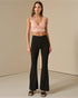 Woman wearing a pink lace top and black flared pants on a beige background