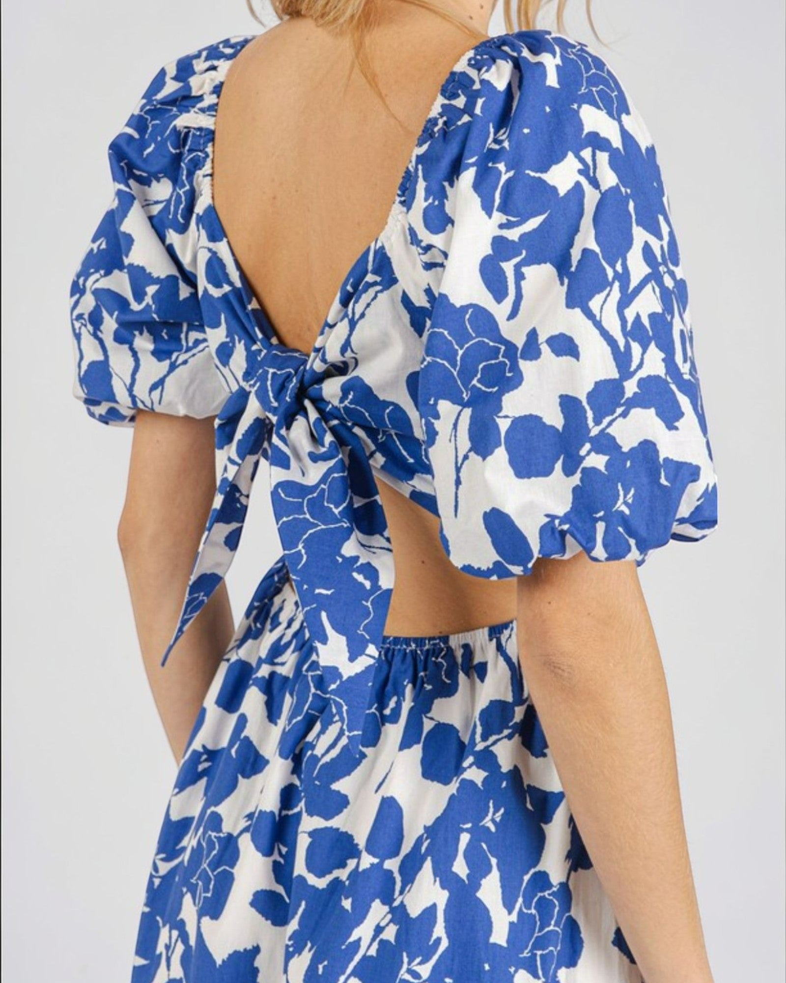 Blue and white floral dress with open back and puff sleeves on a plain background