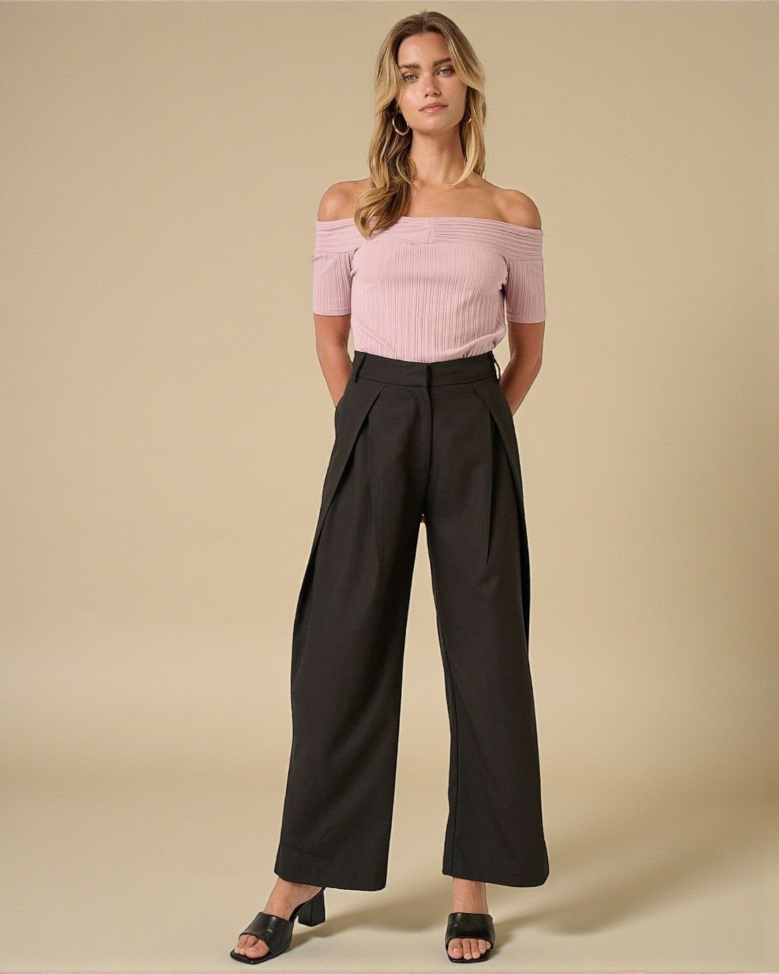 Woman wearing a pink off-shoulder top and black wide-leg pants on a beige background