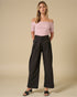 Woman wearing a pink off-shoulder top and black wide-leg pants on a beige background