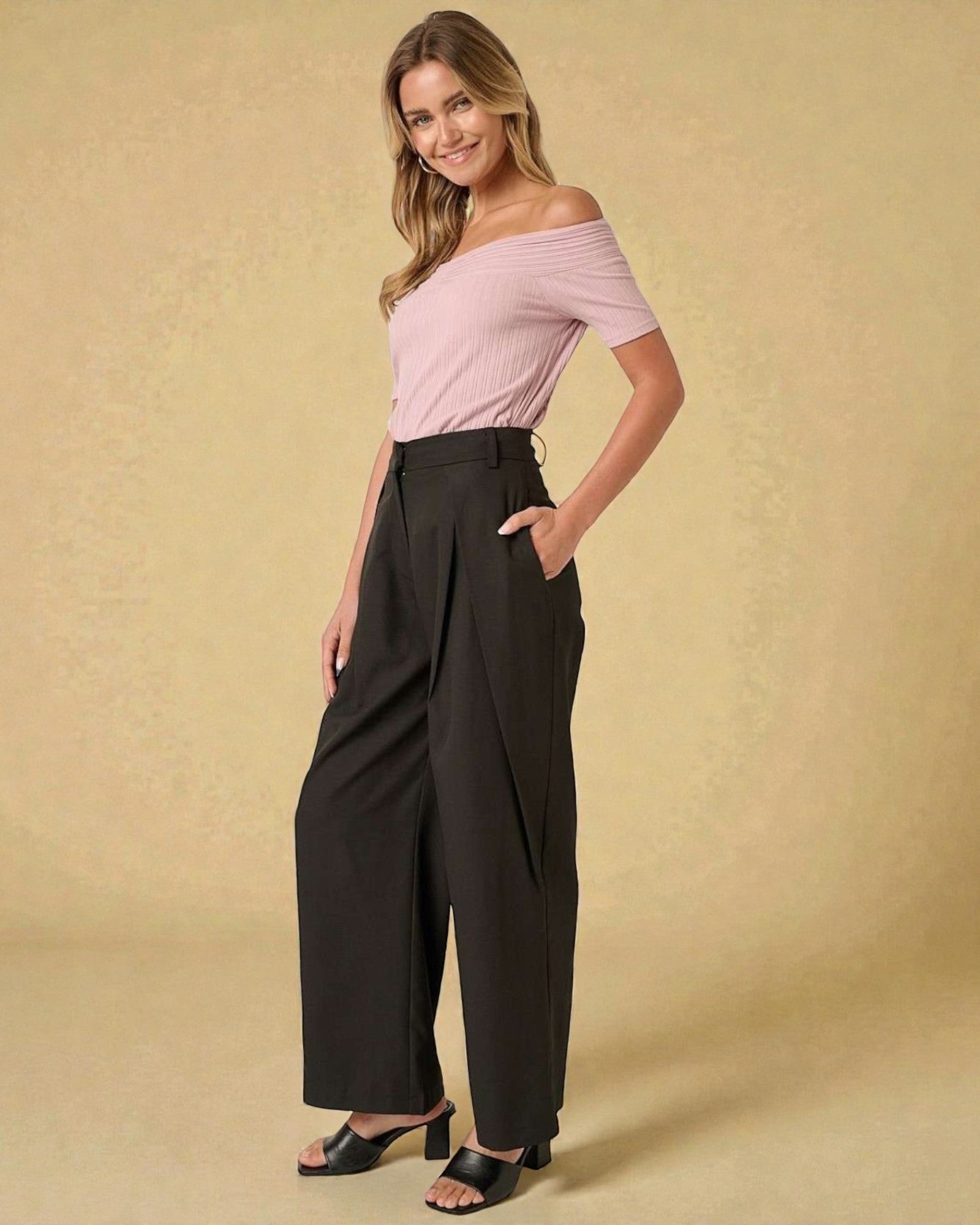 Woman wearing a pink off-shoulder top and black wide-leg pants on a beige background