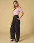 Woman wearing a pink off-shoulder top and black wide-leg pants on a beige background