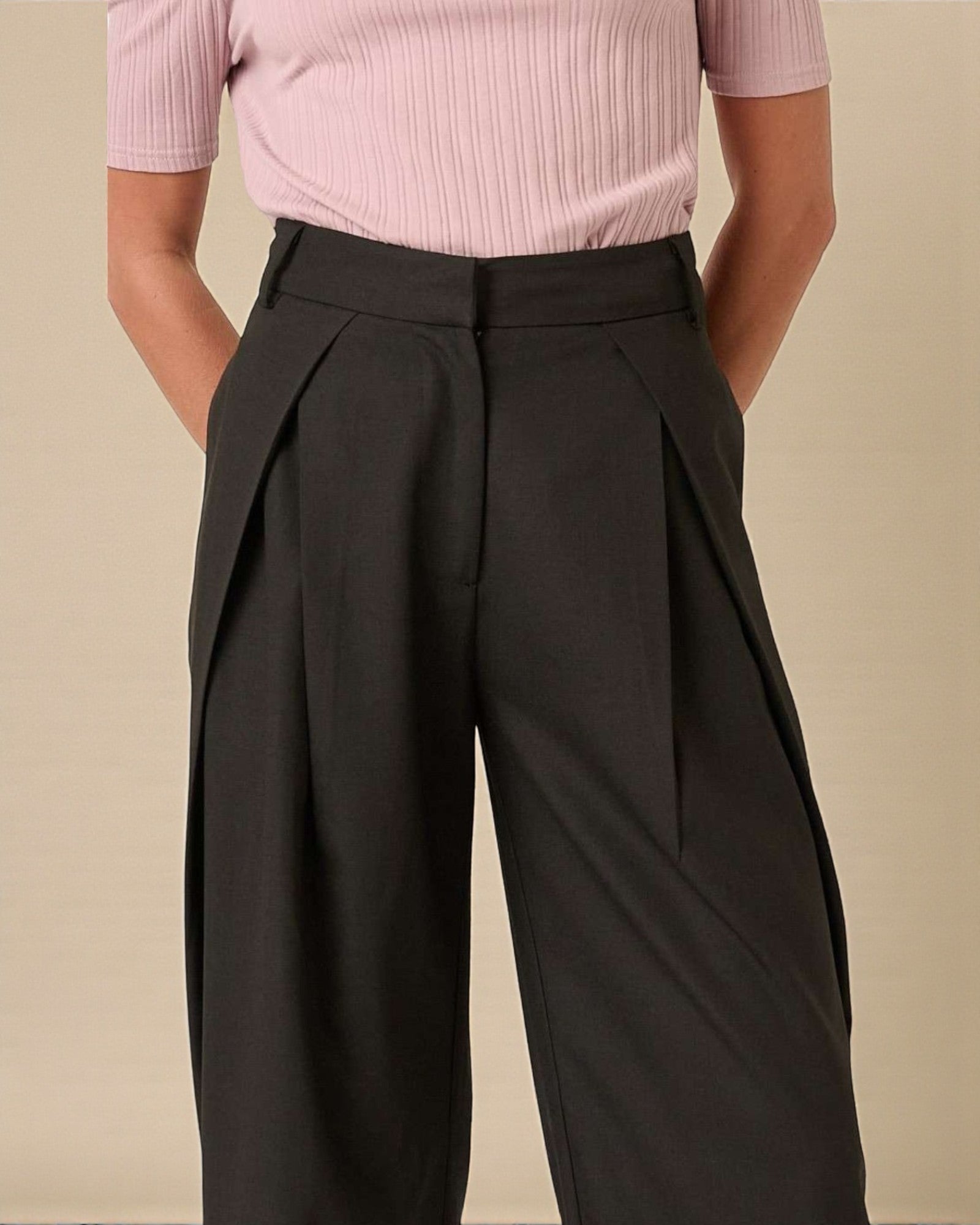 Person wearing a pink pleated top and black wide-leg pants on a beige background