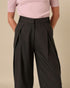 Person wearing a pink pleated top and black wide-leg pants on a beige background