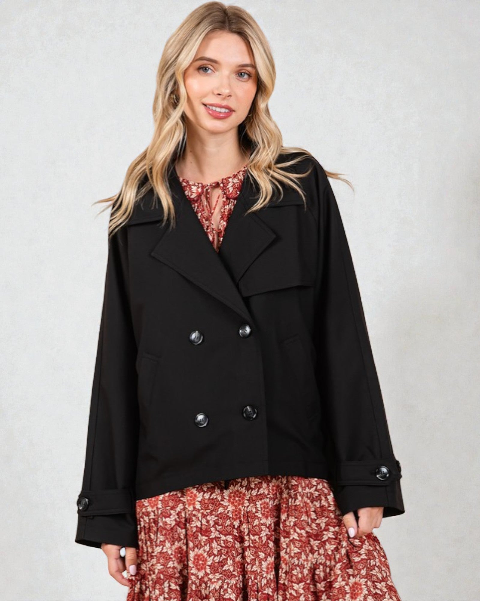 Woman wearing a black coat over a floral dress on a plain background