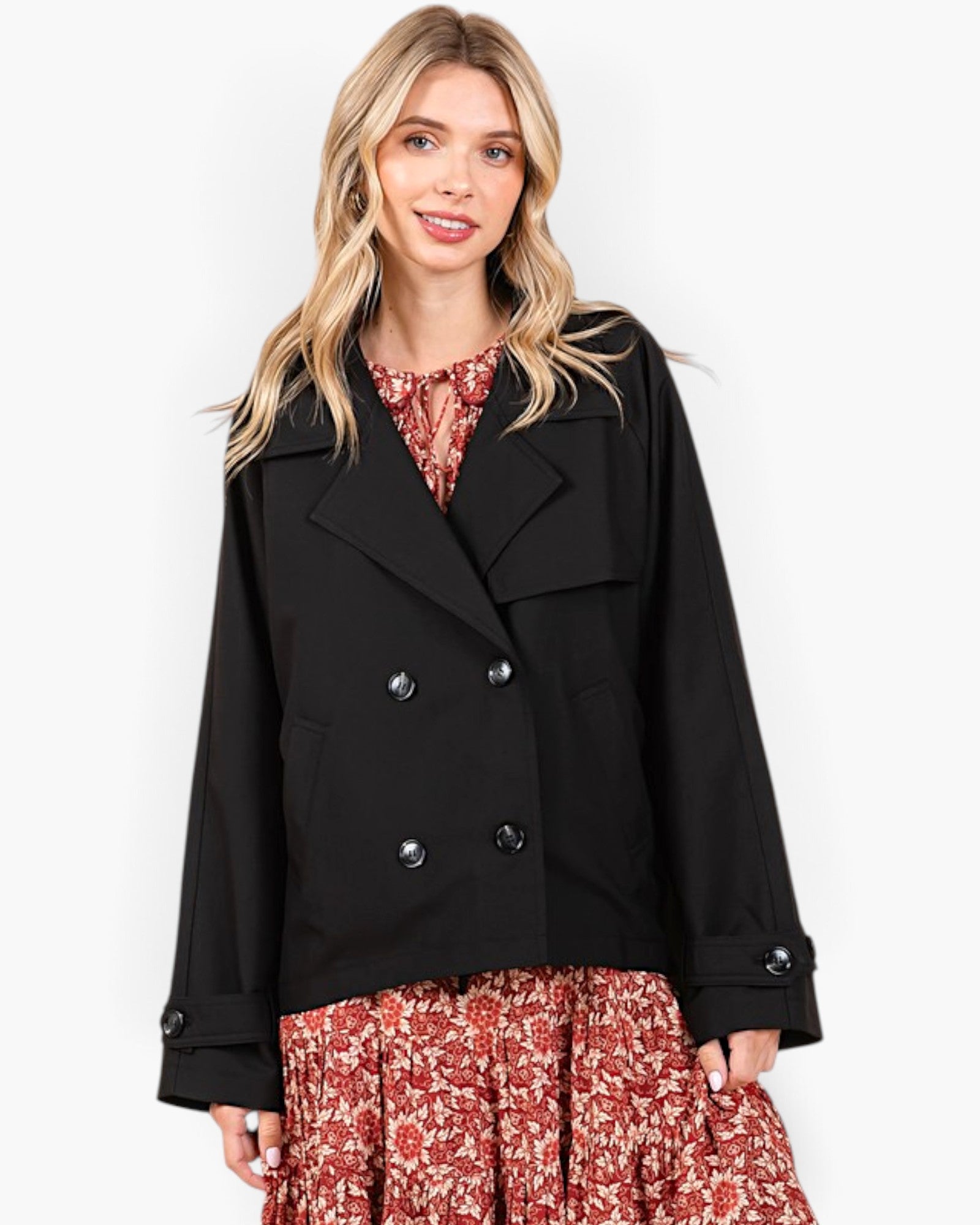A woman modeling a black double-breasted peacoat over a red and white floral dress, photographed against a clean white studio background.