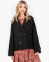 A woman modeling a black double-breasted peacoat over a red and white floral dress, photographed against a clean white studio background.