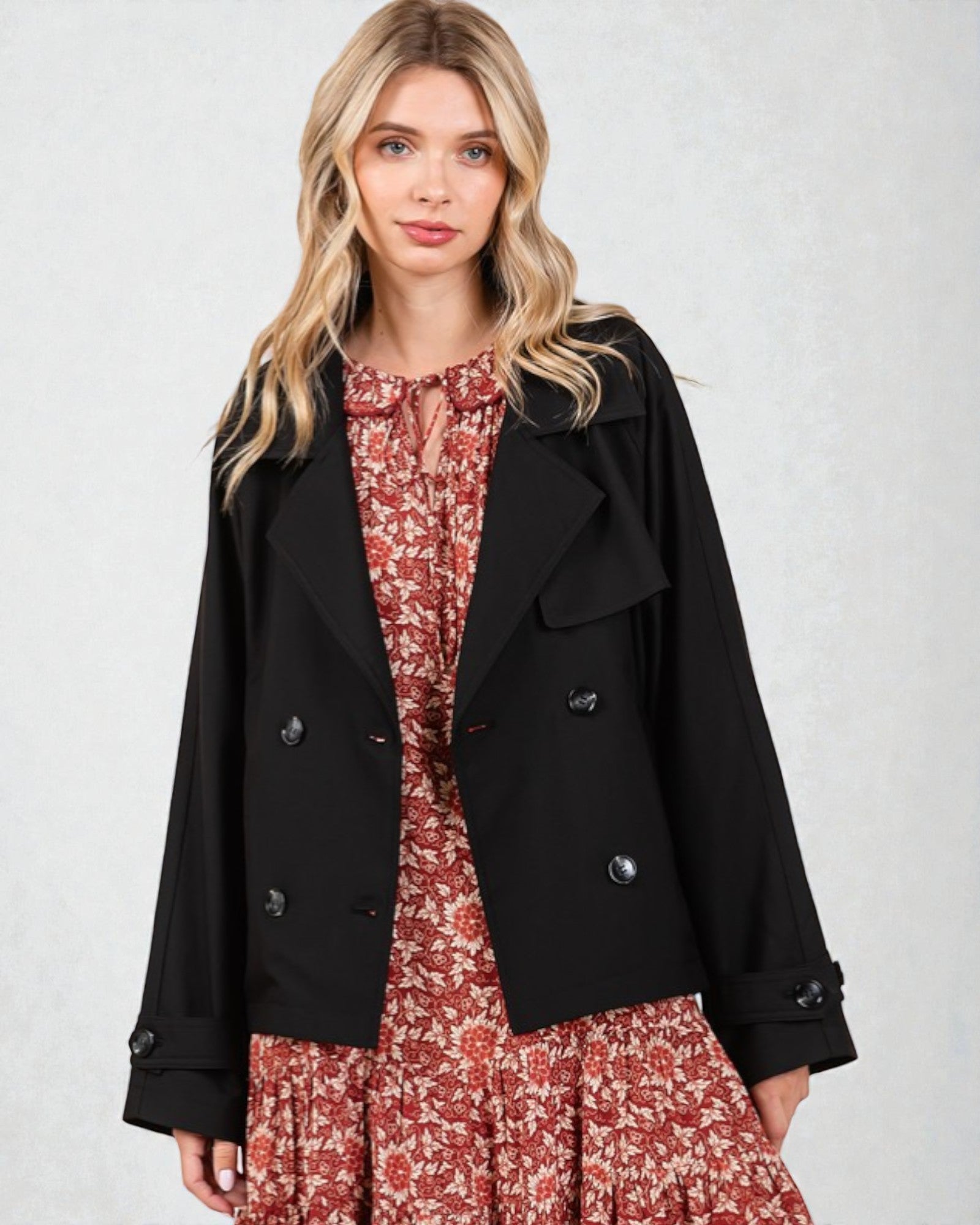 Woman wearing a black coat over a red floral dress on a white background