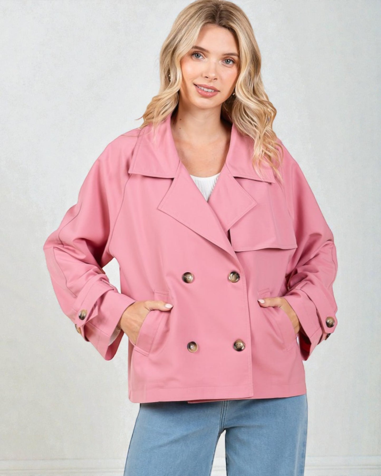 Woman wearing a pink jacket with gold buttons on a plain background