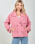 Woman wearing a pink jacket with gold buttons on a plain background
