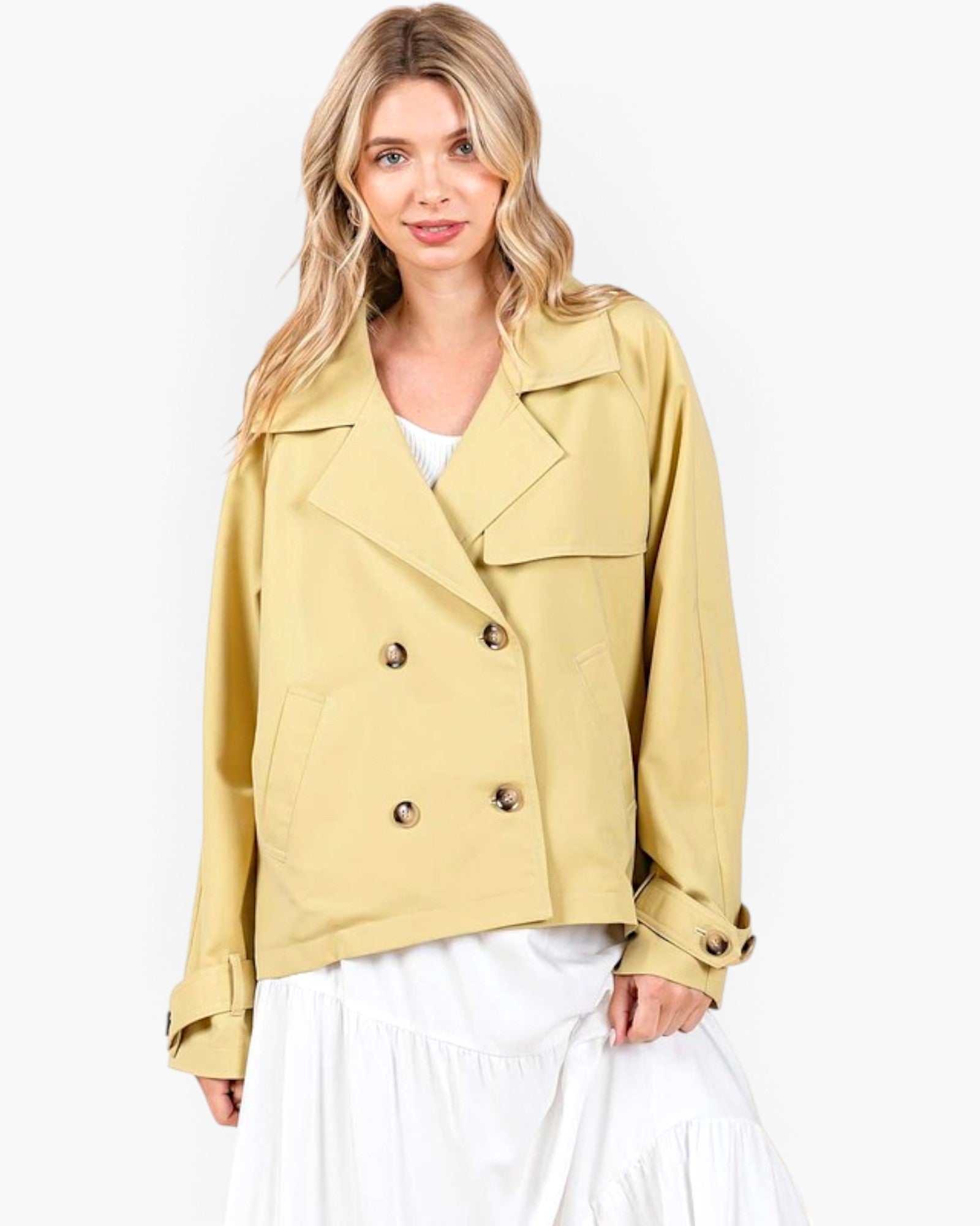 A woman modeling a cropped, double-breasted blazer in a light mustard yellow color, styled with a white top and white skirt against a plain white studio background.